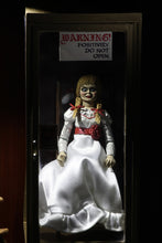 Load image into Gallery viewer, annabelle figure sitting in chair wearing white dress with hair in pig tails. sign reading "warning! positively do not open"