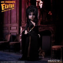 Load image into Gallery viewer, front view of Elvira Living Dead Doll, with iconic black dress and batty, teased hair, and comes with a dagger that she can store in her waist belt. Stands 10” tall and features 5 points of articulation. Packaged in window box for display.