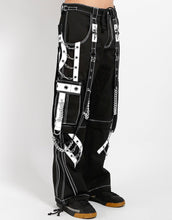 Load image into Gallery viewer, side of Black and white pants feature white stitching, removable straps, adjustable ankles, D-rings, clasps, and deep pockets.