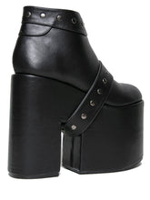 Load image into Gallery viewer, side view of black vegan leather super tall 6" heel, 4" platform sleep design boot. Boot has a rivet studded strap that wraps around and is removable or attachable with Velcro. Boot has black EVA platform.