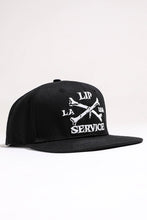 Load image into Gallery viewer, front view of Black hat with white embroidery that reads "LIP SERVICE LA USA" on the front with crossbones. Snaps on the back.