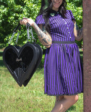 Load image into Gallery viewer, model holding heart shaped glossy black bag with a stitched spiderweb design at the bottom, chain link hardware and faux leather straps.
