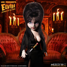 Load image into Gallery viewer, front view of Elvira Living Dead Doll, with iconic black dress and batty, teased hair, and comes with a dagger that she can store in her waist belt. Stands 10” tall and features 5 points of articulation. Packaged in window box for display.

