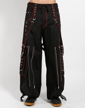 Load image into Gallery viewer, Black classic fit Tripp pants with red stitching, zipper details, removable straps on the back, drawstrings near the feet to tighten the fit, and red skulls printed on the back of each leg.
