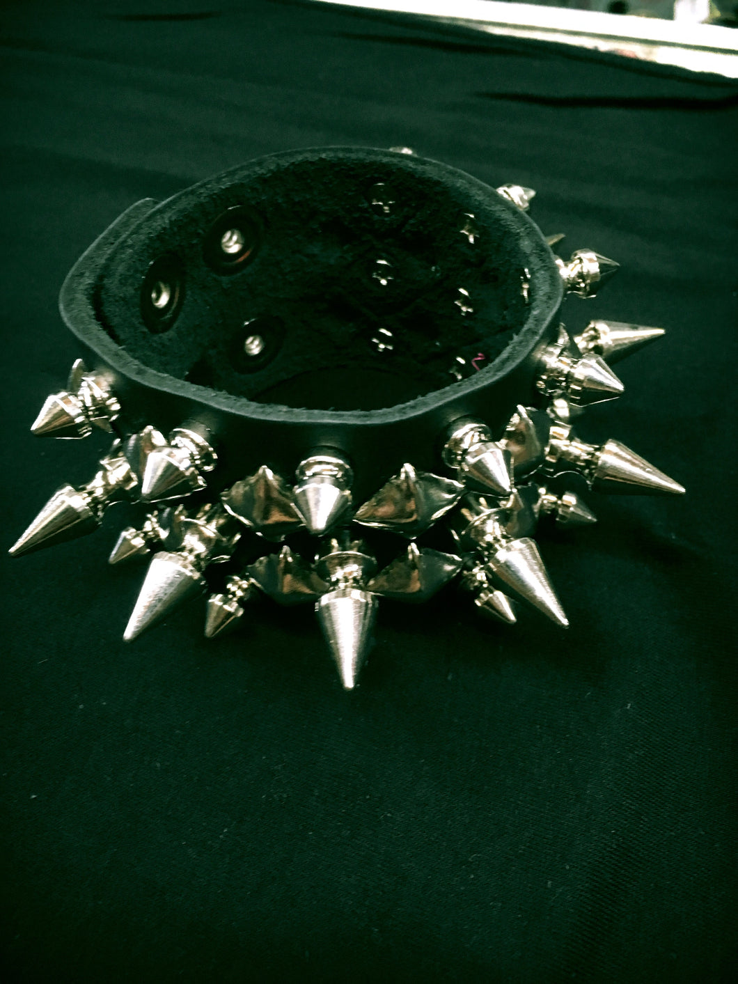 black leather bracelet with three rows of small and large silver spikes and two rows of silver pyramid studs. shows snap closure