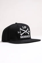 Load image into Gallery viewer, front view of Black hat with white embroidery that reads &quot;LIP SERVICE LA USA&quot; on the front with crossbones. Snaps on the back.

