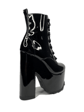 Load image into Gallery viewer, outer view of Black vegan shiny patent leather tall military style platform boot with black cotton laces and black inner zipper. Front of platform has a fanned grip for better stability when walking.

