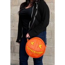 Load image into Gallery viewer, woman wearing bag on shoulder. bag is orange with yellow eyes and yellow teeth, with a black adjustable strap. based on sam&#39;s jack o lantern in the movie trick r&#39; treat
